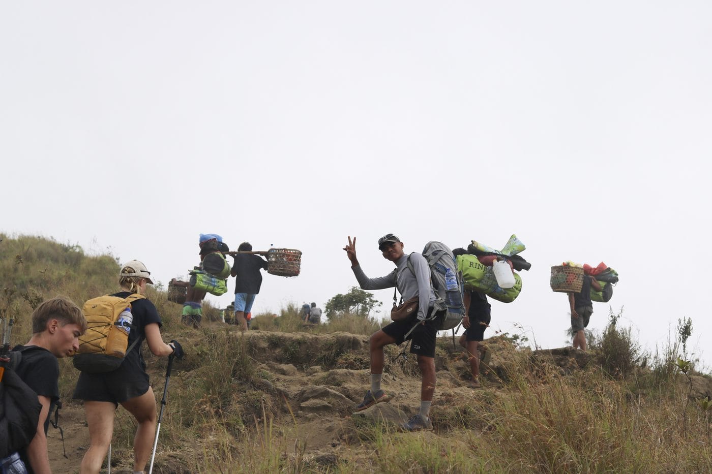 Porters carrying baskets and packs up the ridge while trekkers follow behind with only daypacks